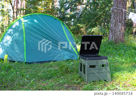 Portable camping toilet in front of tent, field area usage, outdoor comfort and convenience, tourism and travel facility in nature. 140085718
