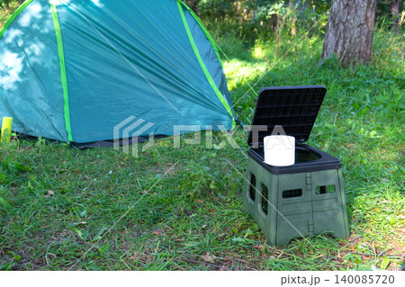Portable toilet and tissue by green tent, outdoor hygiene, camping comfort, convenience for travel, field tourism, area facility. 140085720