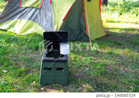 Portable toilet standing on campsite grass in front of tent, camping facility for outdoor use, travel comfort and hygiene in nature tourism. Portable toilet standing on campsite grass in front of tent, camping facility for outdoor use, travel comfort and hygiene in nature tourism. 140085724