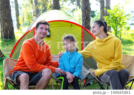 Mom, dad and daughter together by tent, smiling, sports clothing and picnic, summer camping, healthy vacation. 140085861