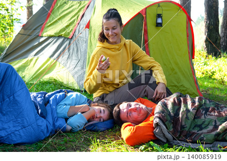 Mother with children in tent, spraying mosquito repellent, healthy camping vacation, bite prevention, safety for family group. 140085919