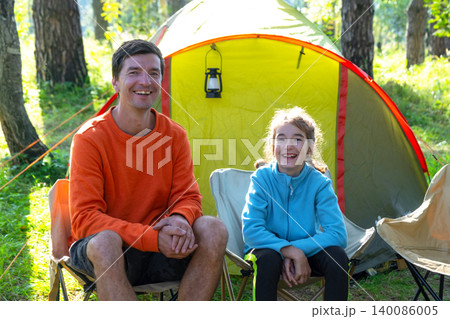 Dad and daughter with tent and chairs, family moments in nature, sports outfits, vacation leisure and camping. Dad and daughter with tent and chairs, family moments in nature, sports outfits, vacation leisure and camping. 140086005