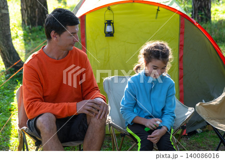 Father and daughter talking about mosquito spray in camping chair, focusing on family health, bite allergy risks, protective parenting, child safety in summer nature. Father and daughter talking about mosquito spray in camping chair, focusing on family health, bite allergy risks, protective parenting, child safety in summer nature. 140086016