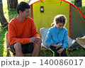 Father handing mosquito repellent to daughter, child protected outdoors, family by tent, allergy and illness prevention, caring emotions, summer adventure. 140086017