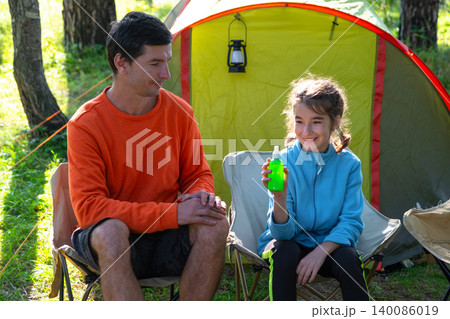Father and daughter enjoying camping, using mosquito spray, focus on child safety, allergy and disease risk, furniture outdoors, joyful family experience. Father and daughter enjoying camping, using mosquito spray, focus on child safety, allergy and disease risk, furniture outdoors, joyful family experience. 140086019