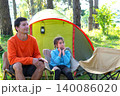 Dad and daughter in tent: family reading book, camping comfort, sportswear, green forest, outdoor rest and fun. 140086020