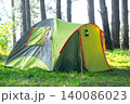 Yellow grey tent in sunlit pine forest, camping ground for tourism, outdoor travel, leisure and adventure applications, recreational area. 140086023
