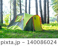Pair of yellow-green tents under tall pine trees, campsite for outdoor tourism, travel leisure, nature adventure and recreation. 140086024