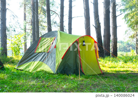 Pair of yellow-green tents under tall pine trees, campsite for outdoor tourism, travel leisure, nature adventure and recreation. Pair of yellow-green tents under tall pine trees, campsite for outdoor tourism, travel leisure, nature adventure and recreation. 140086024