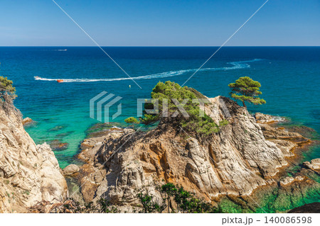Rocky Mediterranean islet with turquoise water and speedboat trail in Lloret de Mar 140086598