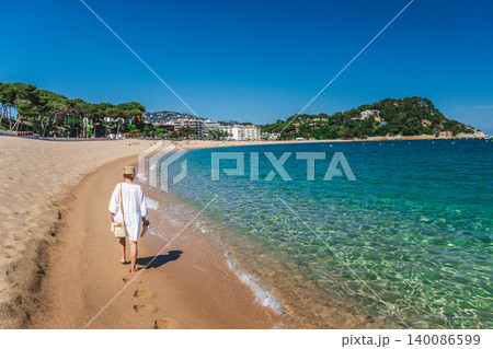 Woman strolling along sandy beach in Lloret de Mar with turquoise Mediterranean water 140086599