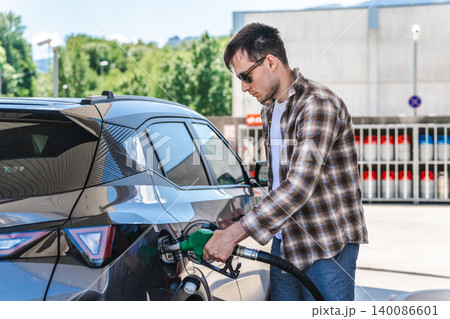 Young man refueling modern crossover vehicle at self service gas station 140086601
