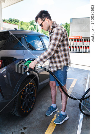 Young man refueling modern crossover vehicle at self service gas station 140086602