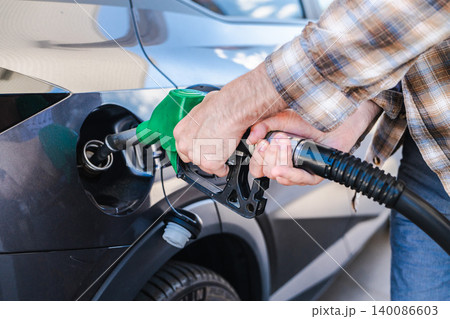 Person refueling modern passenger car at gas station with green fuel nozzle Person refueling modern passenger car at gas station with green fuel nozzle 140086603
