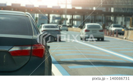 Grey sedan drives along a wide modern multi lane highway during the day. Other white cars travel ahead on the clean asphalt road surface beneath an ahead is a toll booth for the expressway. Grey sedan drives along a wide modern multi lane highway during the day. Other white cars travel ahead on the clean asphalt road surface beneath an ahead is a toll booth for the expressway. 140086731