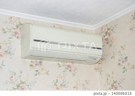 Wall-Mounted Split Air Conditioner Over Floral Wallpapered Corner Ceiling in Vintage Home Interior 140086818