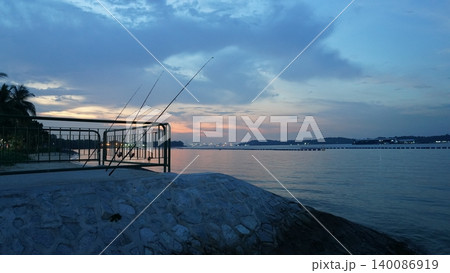 Idyllic Coastal Sunset with Fishing Rods and Palm Trees Idyllic Coastal Sunset with Fishing Rods and Palm Trees 140086919