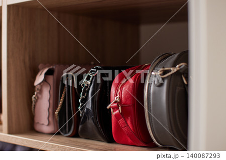 Collection of stylish women's fashion handbags sitting neatly on a wooden shelf, organizing accessories in an elegant closet 140087293