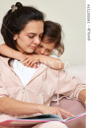 Mother and daughter embracing while reading a book. Childhood education, family bonding, and loving parenting moments at home 140087334