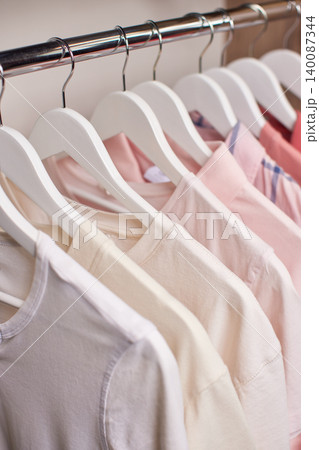 Row of various shirts hanging on white hangers on a metal rail inside a closet, showing organization and neatness Row of various shirts hanging on white hangers on a metal rail inside a closet, showing organization and neatness 140087344