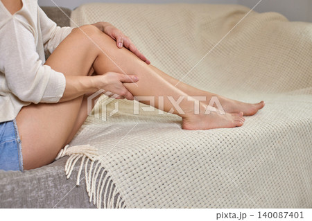 Woman sitting on a sofa massaging her shin and calf to relieve muscle pain, cramp, or exhaustion after exercise Woman sitting on a sofa massaging her shin and calf to relieve muscle pain, cramp, or exhaustion after exercise 140087401