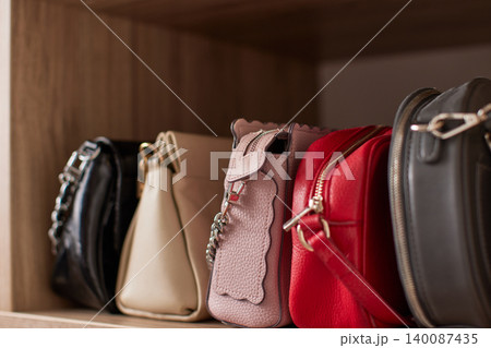 Collection of stylish women's fashion handbags sitting neatly on a wooden shelf, organizing accessories in an elegant closet 140087435