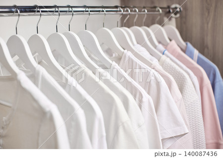 Clothes hanging on white wooden hangers in a neat wardrobe. Displaying minimalist fashion and organized storage Clothes hanging on white wooden hangers in a neat wardrobe. Displaying minimalist fashion and organized storage 140087436