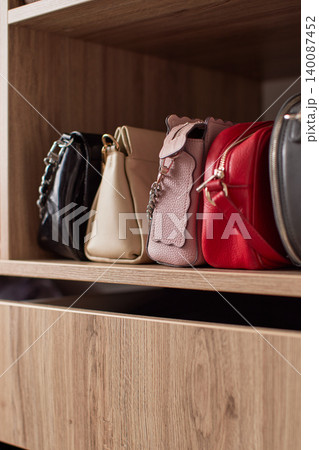 Collection of stylish women's fashion handbags sitting neatly on a wooden shelf, organizing accessories in an elegant closet Collection of stylish women's fashion handbags sitting neatly on a wooden shelf, organizing accessories in an elegant closet 140087452