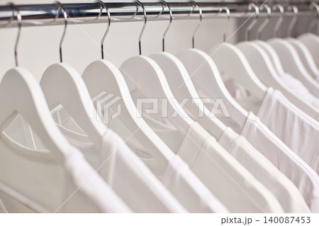 Clean white t-shirts neatly hanging inside a wardrobe on wooden hangers, showing freshness and organization 140087453
