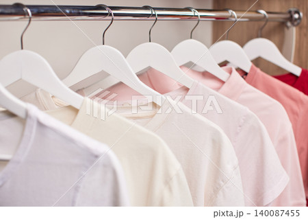 Clothing rail of neatly arranged pastel pink ombre t-shirts on white hangers, minimalist wardrobe display for boutique or closet photography 140087455