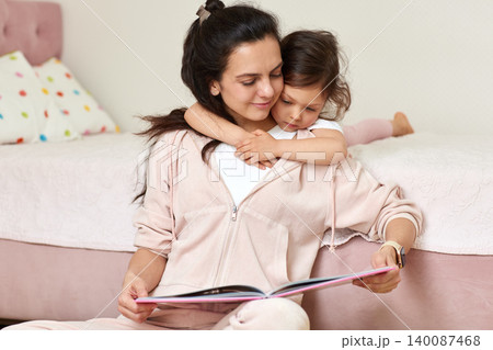 Mother reading a storybook to daughter, sharing a moment of bonding, love, and education in a cozy home setting Mother reading a storybook to daughter, sharing a moment of bonding, love, and education in a cozy home setting 140087468