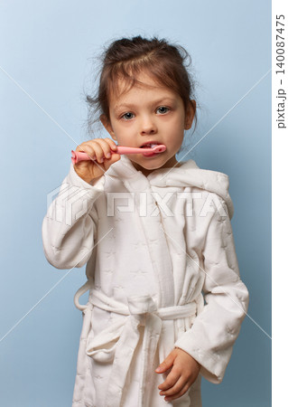 child girl brushing teeth wearing white bathrobe promoting hygiene, daily dental care and routine 140087475