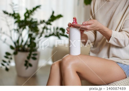 Woman dispensing moisturizing lotion from a pump bottle into her hand, reflecting self-care and beauty ritual 140087489