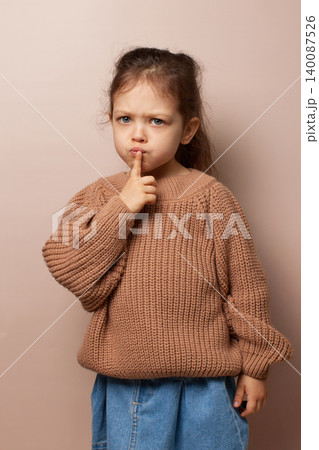 Young child girl with finger on lips asking for quiet with thoughtful expression on beige background Young child girl with finger on lips asking for quiet with thoughtful expression on beige background 140087526
