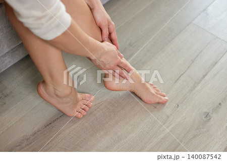 Woman experiencing leg pain and discomfort, massaging her aching ankle and tired feet at home, seeking relief Woman experiencing leg pain and discomfort, massaging her aching ankle and tired feet at home, seeking relief 140087542