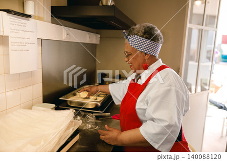 Smiling Senior Black Woman Preparing Individual Savory Pies in Professional Bakery Kitchen Smiling Senior Black Woman Preparing Individual Savory Pies in Professional Bakery Kitchen 140088120