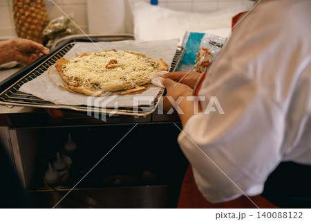 Middle aged Black cook holding raw cheese pizza on baking rack in kitchen 140088122