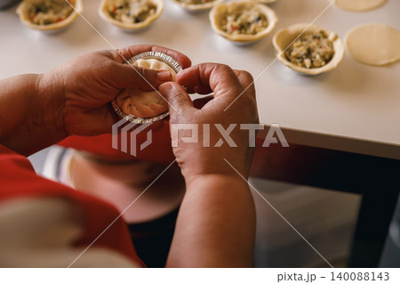 Mature Black woman hands carefully preparing mini savory pies on a kitchen counter at home. Mature Black woman hands carefully preparing mini savory pies on a kitchen counter at home. 140088143