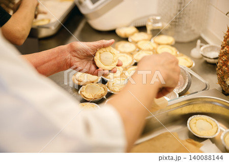 Caucasian senior baker preparing small dough pastries in a commercial kitchen Caucasian senior baker preparing small dough pastries in a commercial kitchen 140088144