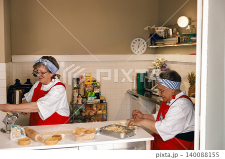 Senior Caucasian and Black women cooking fresh pasta and pastries in a bright kitchen setting Senior Caucasian and Black women cooking fresh pasta and pastries in a bright kitchen setting 140088155