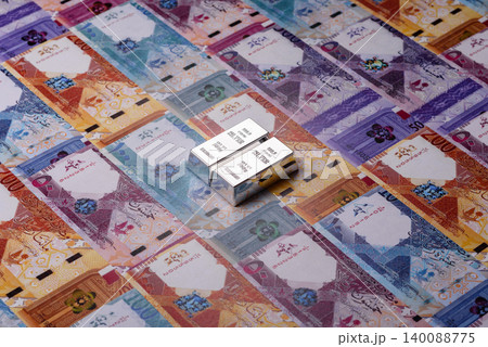 A silver bar, white metal against a backdrop of Qatari money, as a concept. A silver bar A silver bar, white metal against a backdrop of Qatari money, as a concept. A silver bar 140088775