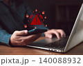 Man holding phone with red warning triangle icon. Cyber security concept of secure data protection failure. Hacking, phishing scam, and ransomware malware risk on laptop background. 140088932