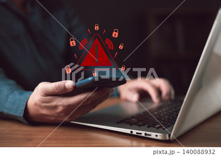 Man holding phone with red warning triangle icon. Cyber security concept of secure data protection failure. Hacking, phishing scam, and ransomware malware risk on laptop background. 140088932