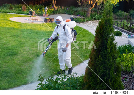 Spring garden pest control: man in protective suit spraying plants Spring garden pest control: man in protective suit spraying plants 140089043