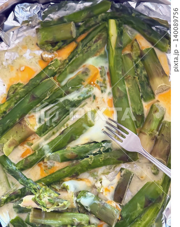 Baked asparagus with eggs and melted cheese sits on foil with fork in close food preparation scene. Top view of asparagus meal, cooking, diet, nutrition, kitchen dinner, home recipe 140089756