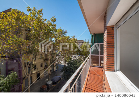 A sunny balcony view overlooking a tree-lined street in an urban area. Bright blue sky and modern buildings are visible A sunny balcony view overlooking a tree-lined street in an urban area. Bright blue sky and modern buildings are visible 140090043