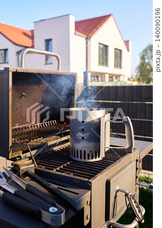 Open grill with charcoal chimney and smoke stands in backyard Open grill with charcoal chimney and smoke stands in backyard 140090196