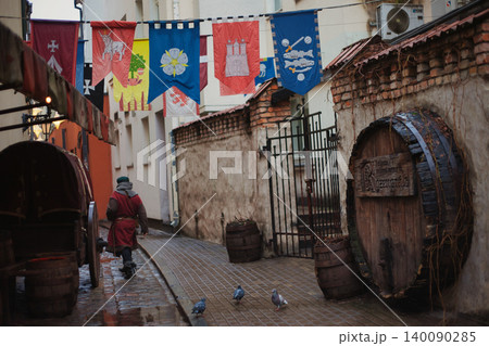 Medieval-style street scene with colorful heraldic banners suspended over a wet cobblestone alley Medieval-style street scene with colorful heraldic banners suspended over a wet cobblestone alley 140090285