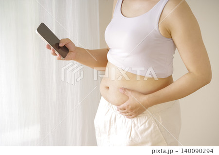 スマホを持ちお腹まわりを気にする女性 スマホを持ちお腹まわりを気にする女性 140090294