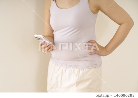 スマホを持ちお腹まわりを気にする女性 スマホを持ちお腹まわりを気にする女性 140090295